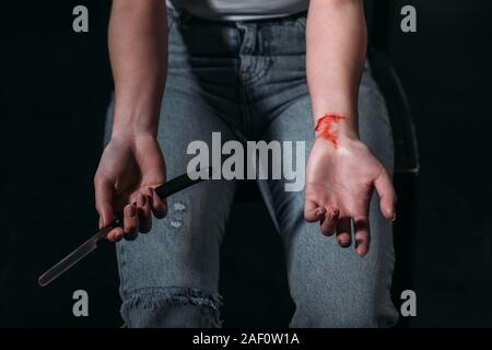 Vista ritagliata della giovane donna di suicidarsi dal taglio di vene con rasoio su sfondo scuro Foto Stock