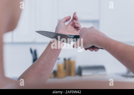 Vista ritagliata della depressione donna suicidio da vene di taglio con il coltello in cucina Foto Stock