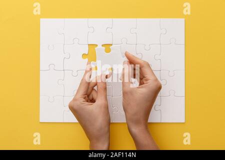 Vista ritagliata della donna che mantiene il pezzo di bianco puzzle su sfondo giallo Foto Stock