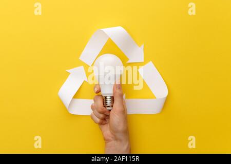 Vista ritagliata della donna tenendo la lampadina della luce di carta sotto il triangolo di artigianato su sfondo giallo Foto Stock