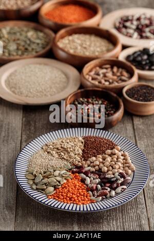 Piastra a strisce con le lenticchie, fagioli, ceci, i cereali e i semi di zucca vicino a ciotole di legno sul tavolo Foto Stock