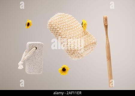 Spazzolino da denti, pietra pomice, vasca da bagno in spugna e fiori di colore giallo isolato su grigio Foto Stock