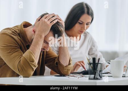 Triste e uomo bello tenendo la testa e donna attraente utilizzando la calcolatrice Foto Stock