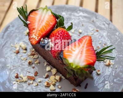 Close-up e la vista in pianta di una deliziosa torta al cioccolato guarnita con un pezzo di fragole e bacche su grigio piatto di ceramica dello sfondo. Foto Stock