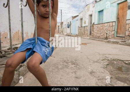 Penedo, Alagoas, Brasile - 04 luglio 2016: Piccolo ragazzo seduto al cancello d'ingresso della sua casa in un quartiere povero intorno al centro di Penedo Foto Stock