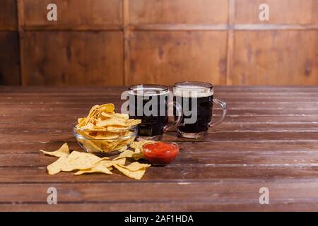 Due boccali di birra con spuntini sul tavolo di legno Foto Stock