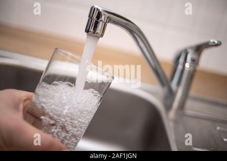 Duesseldorf, Germania. Decimo Dec, 2019. Illustrazione - un uomo tiene un bicchiere sotto l'acqua corrente. Il Bündnis 90/Die Grünen i commenti del gruppo sulla base dei risultati di un'inchiesta sull'acqua nel NRW. Una delle questioni in gioco è lo sviluppo di acqua per uso domestico di consumo. Credito: Marius Becker/dpa/Alamy Live News Foto Stock