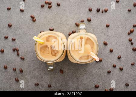 Vista superiore del caffè ghiacciato in vasi di vetro con cannucce e caffè in chicchi su sfondo grigio Foto Stock