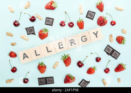 Vista superiore dei blocchi di legno con allergia scritte nei pressi di ciliegie, dadi, fragole e cioccolato isolato su blu Foto Stock