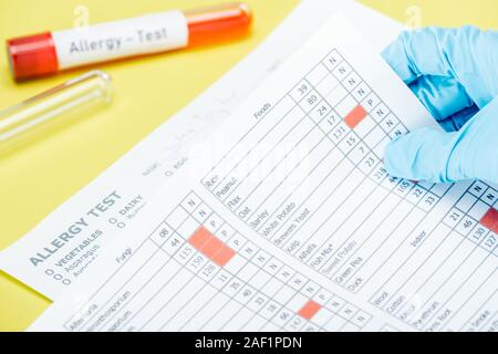 Vista ritagliata della donna azienda allergia i risultati dei test nei pressi di provette con allergia lettering di test isolato su giallo Foto Stock