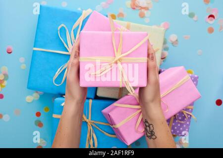 Vista ritagliata della donna rosa azienda confezione regalo vicino colorato presenta nei pressi di coriandoli su blu Foto Stock