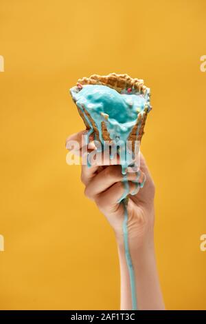 Vista ritagliata della donna azienda blu del fuso di gelato in cialda croccante cono isolato su giallo Foto Stock