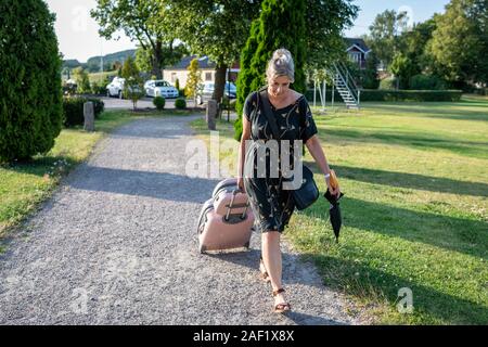 Donna valigia di trazione sul viale di accesso Foto Stock