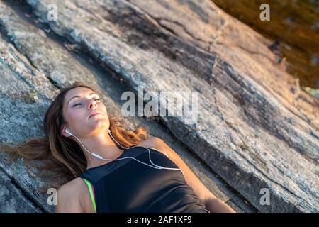 Donna sdraiata su rocce con gli occhi chiusi Foto Stock