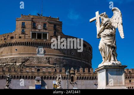 Una statua di un angelo, che porta una croce sul Ponte Sant'Angelo, il castello di Santo Angelo, Castel Sant'Angelo a distanza Foto Stock