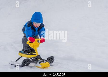 Little Boy cavalca un scooter neve in inverno Foto Stock