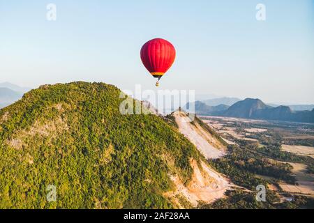 Red mongolfiere volare oltre la montagna e il verde campo di riso in Vang Vieng, Laos Foto Stock