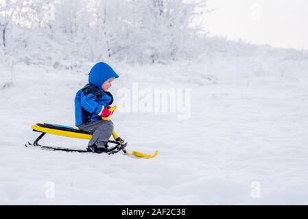 Little Boy cavalca un scooter neve in inverno Foto Stock