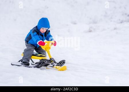 Little Boy cavalca un scooter neve in inverno Foto Stock