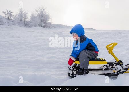 Little Boy cavalca un scooter neve in inverno Foto Stock