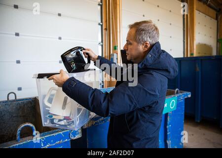 Un uomo mettendo i vecchi apparecchi nel cassonetto nel centro di smistamento per un sicuro smaltimento e riciclaggio Foto Stock
