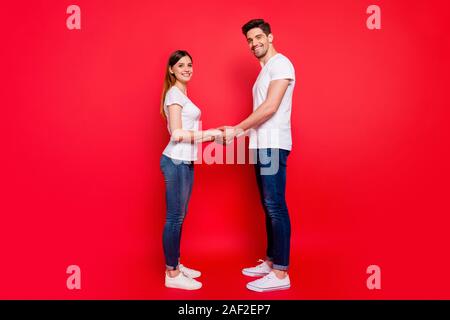 Per tutta la lunghezza del corpo lato di dimensione della foto del profilo di allegro carino bella coppia di coniugi tenendo le mani in jeans denim t-shirt sneakers amarsi Foto Stock