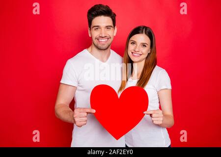 Foto di allegro positivo piuttosto carino bella coppia di coniugi azienda big red t-shirt bianca con cuore toothily sorridente che mostrano il loro amore isolato vivid Foto Stock