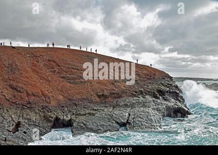 Spettacolare scogliera di El Golfo, Lanzarote con molti turisti in cima e grandi onde che si schiantano nella base della scogliera Foto Stock