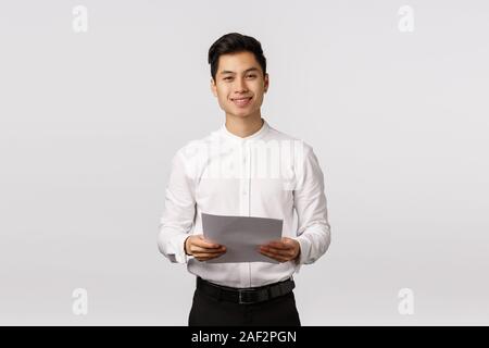 Bello ed elegante giovani asiatici collega maschio, imprenditore nel collare bianco shirt, pantaloni neri, tenendo le carte e sorridente fotocamera, imprenditore di successo Foto Stock