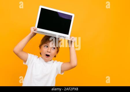 Sorpreso boy può contenere un computer portatile sulla sua testa con un mockup su sfondo giallo con spazio di copia Foto Stock