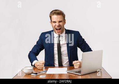 Espressiva e indignato bionda e giovane imprenditore pounding tabella in modo aggressivo e gridando business partner, il sentirsi deluso e sconvolto Con Foto Stock