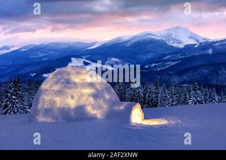 Neve vera casa igloo in inverno le montagne. Coperte di neve abeti e le vette delle montagne sullo sfondo. La nebbia foresta con abete innevato Foto Stock