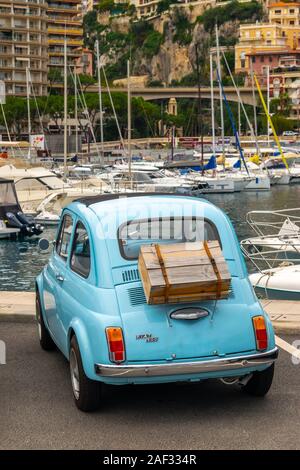 Monaco 5 DIC 2019 vecchio e blu vintage Fiat 500 auto con scatola in legno sulla sua schiena nel porto della città di Monaco e nel paesaggio urbano e yachts sfondo Foto Stock