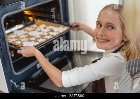 Ragazza posizionando i cookie nel forno aperto Foto Stock