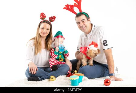 Studio di stock di foto di una coppia con un bambino e un cane seduto sul pavimento dissimulata come il Natale con uno sfondo bianco Foto Stock