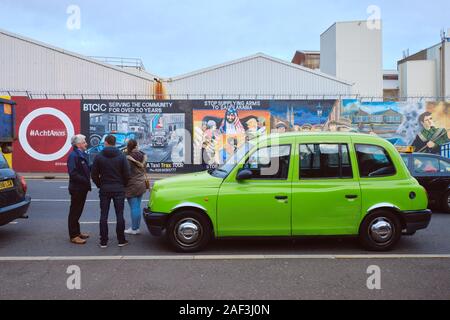 Verde della cabina tradizionale su un tour di Belfast, con driver dando la storia di difficoltà per due turisti di fronte sulla pace art wall Foto Stock