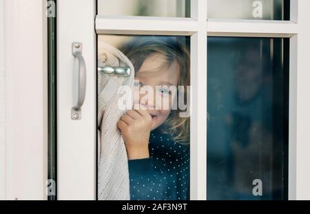 Ragazza giovane cerca attraverso una porta finestra guarda sorridendo felice Foto Stock