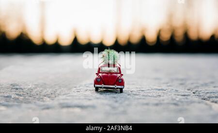 Piccolo rosso Beatle auto con un albero di Natale sulla parte superiore la guida in presenza di neve Foto Stock