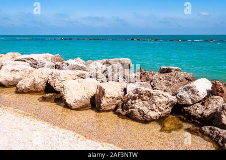 Pietre massicce rocce sdraiato sulla spiaggia come un confine tra la spiaggia ghiaiosa spiaggia del Frate e del mare Adriatico onde e flussi. Rocky marina come una breakw Foto Stock