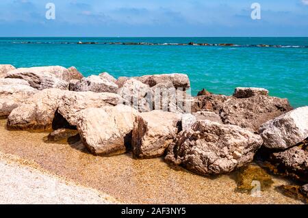 Pietre massicce rocce sdraiato sulla spiaggia come un confine tra la spiaggia ghiaiosa spiaggia del Frate e del mare Adriatico onde e flussi. Rocky marina come una breakw Foto Stock