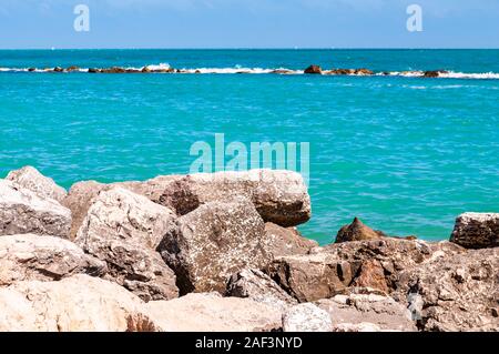 Pietre massicce rocce sdraiato sulla spiaggia come un confine tra la spiaggia ghiaiosa spiaggia del Frate e del mare Adriatico onde e flussi. Rocky marina come una breakw Foto Stock