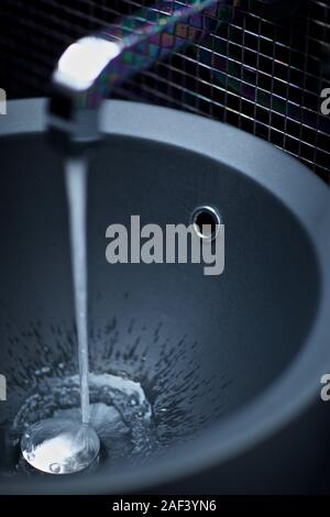 Il flusso di acqua si riversa dal rubinetto del lavandino del bagno Foto Stock