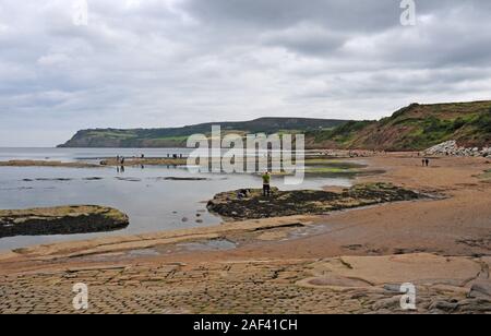 La bassa marea. Robin Hood's Bay. Persone piscine di roccia da esplorazione e alla ricerca di fossili. Foto Stock