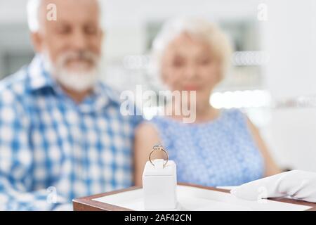 Close up di sorprendenti golden anello con pietra blu che consulente tenendo le mani in guanti bianchi. Senior uomo barbuto acquisto anello esclusivo per sua moglie in negozio Gioielli Foto Stock