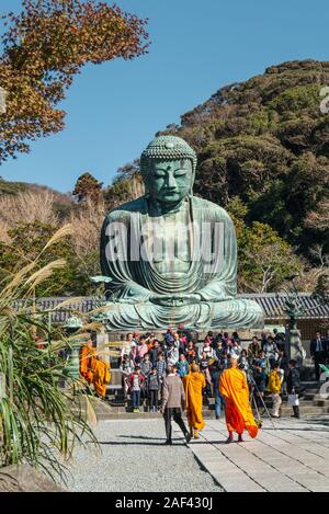 La folla dei turisti e dei monaci buddisti in arancione vesti si raduna per scattare una fotografia al Grande Buddha di Kamakura statua. Foto Stock