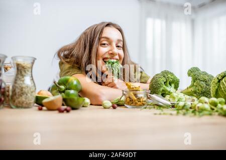 Ritratto di una giovane donna allegra con le piantine di piselli e un sacco di sano cibo verde sul tavolo. Concetto di vegetarianismo e benessere Foto Stock