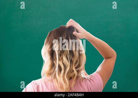 Vista posteriore del giovane donna bionda di graffiare la testa contro lo sfondo di colore verde Foto Stock