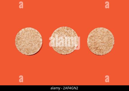 Tre di riso o di mais Biscotti in un'arancia-carota colore di sfondo, vista dall'alto dei biscotti croccanti per il food design e il mangiare sano, spazio di copia Foto Stock