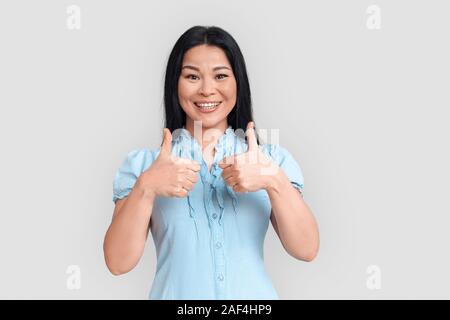 Freestyle. Donna asiatica in piedi isolato su bianco Thumbs up allegro sorridente Foto Stock