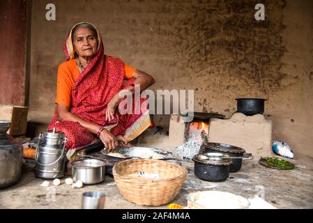 CHIKHALDARA, MAHARASHTRA - Agosto 28, 2018: Un misterioso vecchio donna fare e cucina / cottura di alimenti freschi in un villaggio rurale in una cucina vintage u Foto Stock